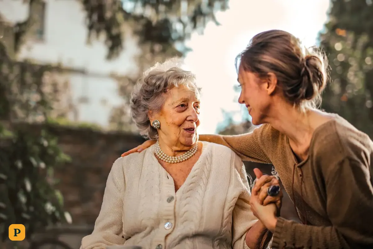 An adult daughter greets her smiling mother in a garden