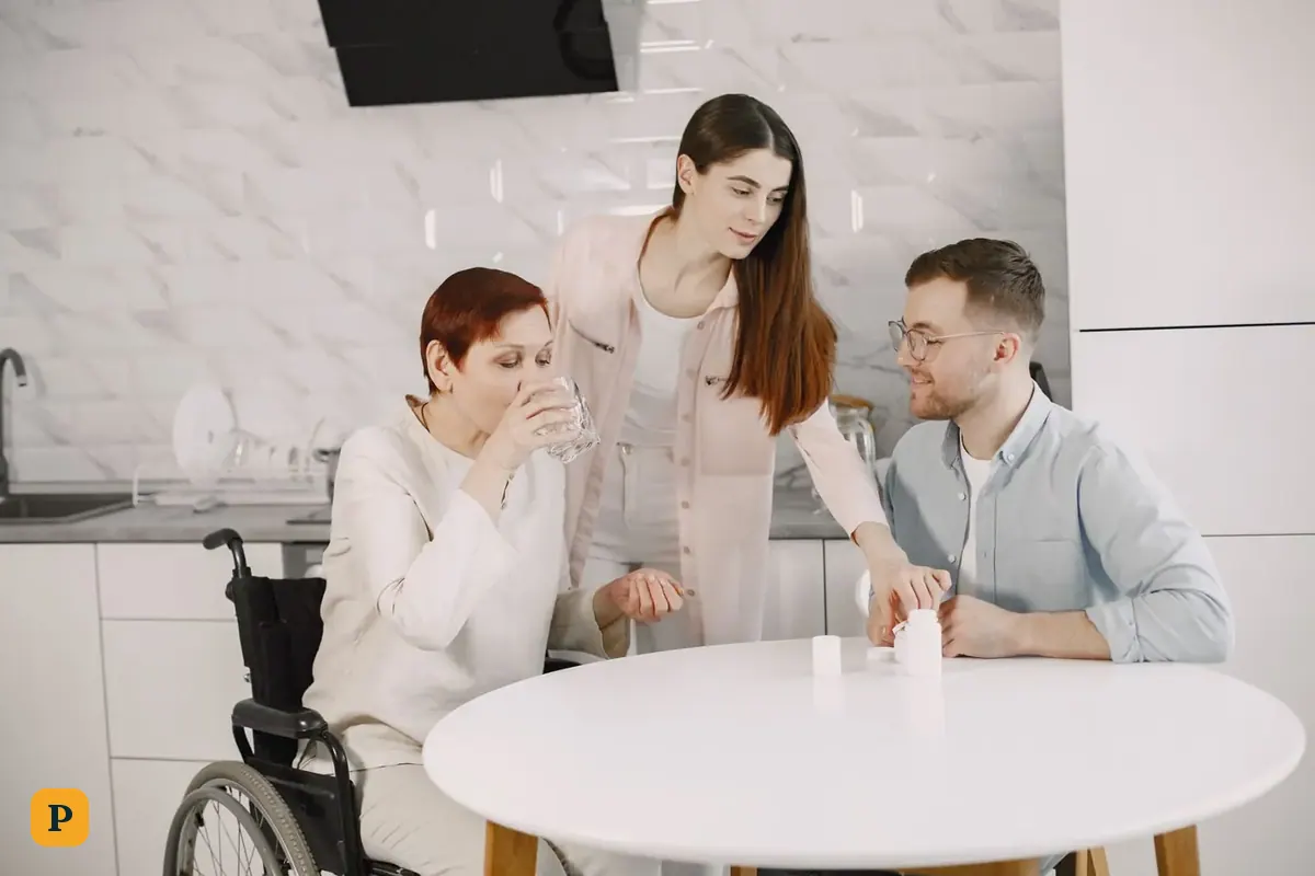 An adult son and daughter help their mother, who uses a wheelchair, with her medicine in the kitchen