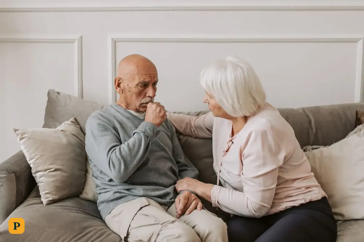 An older woman comforts her husband on the sofa